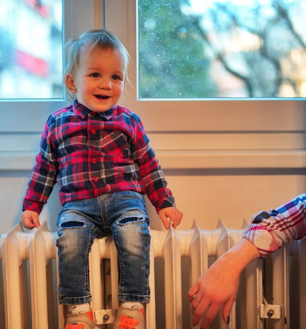 Cute little boy sitting on a radiator against the window